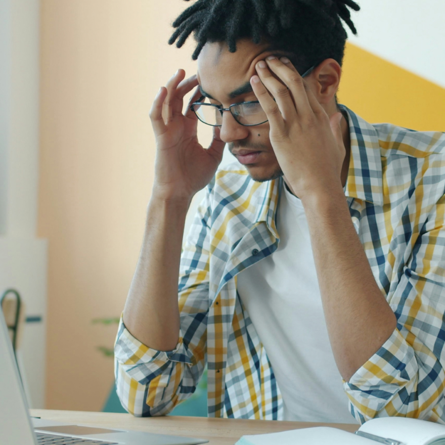 Man with his hands on his temples as he looks at laptop with notebook beside it managing high-functioning anxiety
